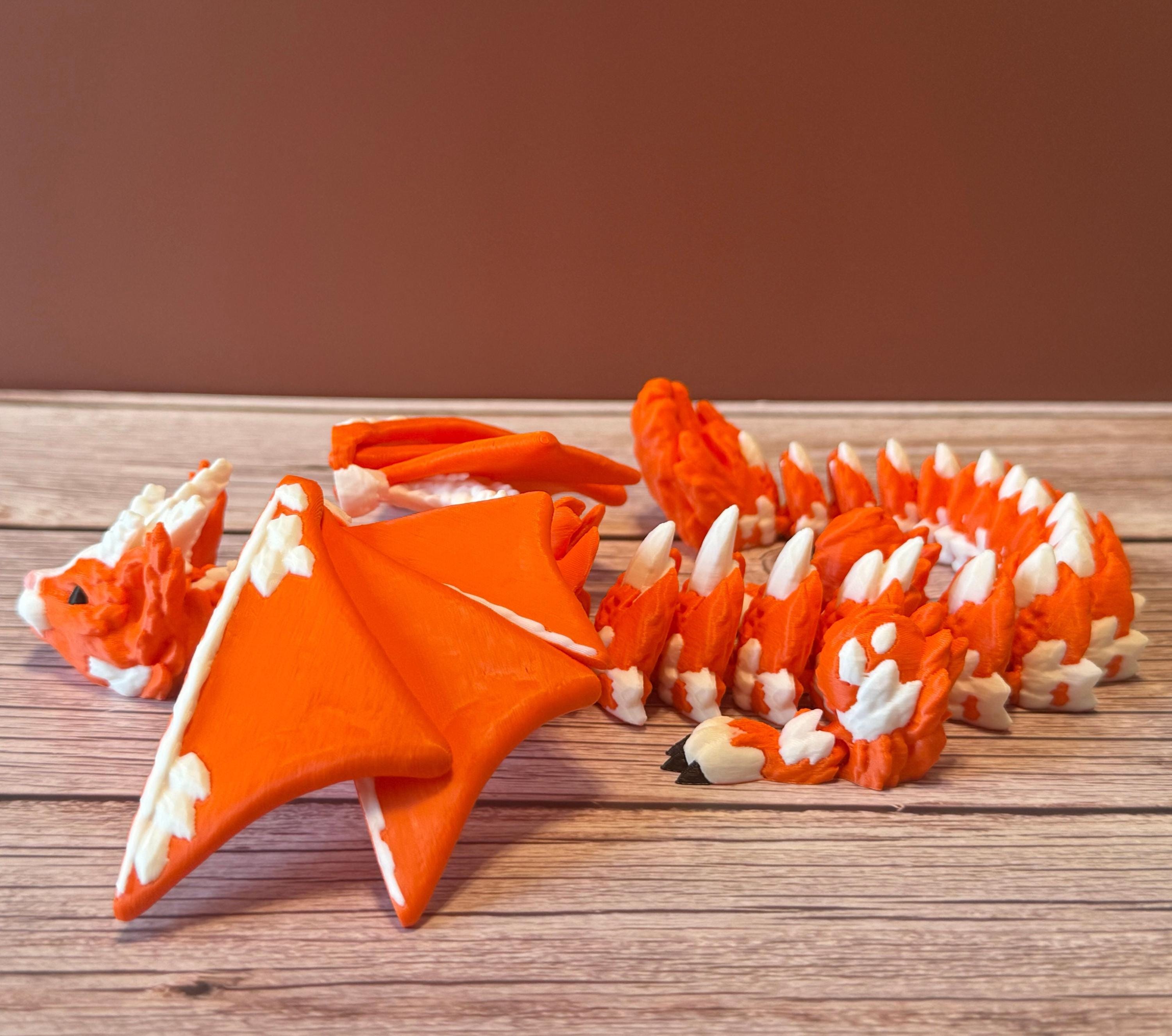 Orange and white 3D printed dragon figurine featuring a hybrid design of a dragon and a cat, placed on a wooden surface