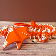 Orange and white 3D printed dragon figurine featuring a hybrid design of a dragon and a cat, placed on a wooden surface