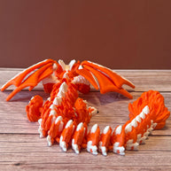 Orange and white 3D printed dragon figurine featuring a hybrid design of a dragon and a cat, placed on a wooden surface