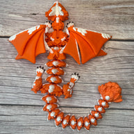 Orange and white 3D printed dragon figurine featuring a hybrid design of a dragon and a cat, placed on a wooden surface