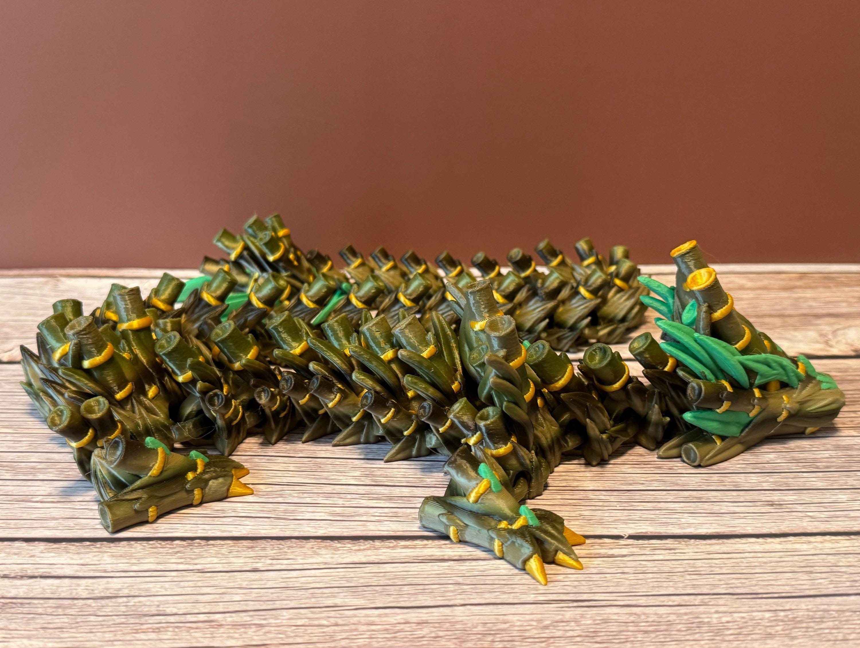 A green, brown, and gold colored 3D printed dragon figure with bamboo-like features, placed on a wooden surface