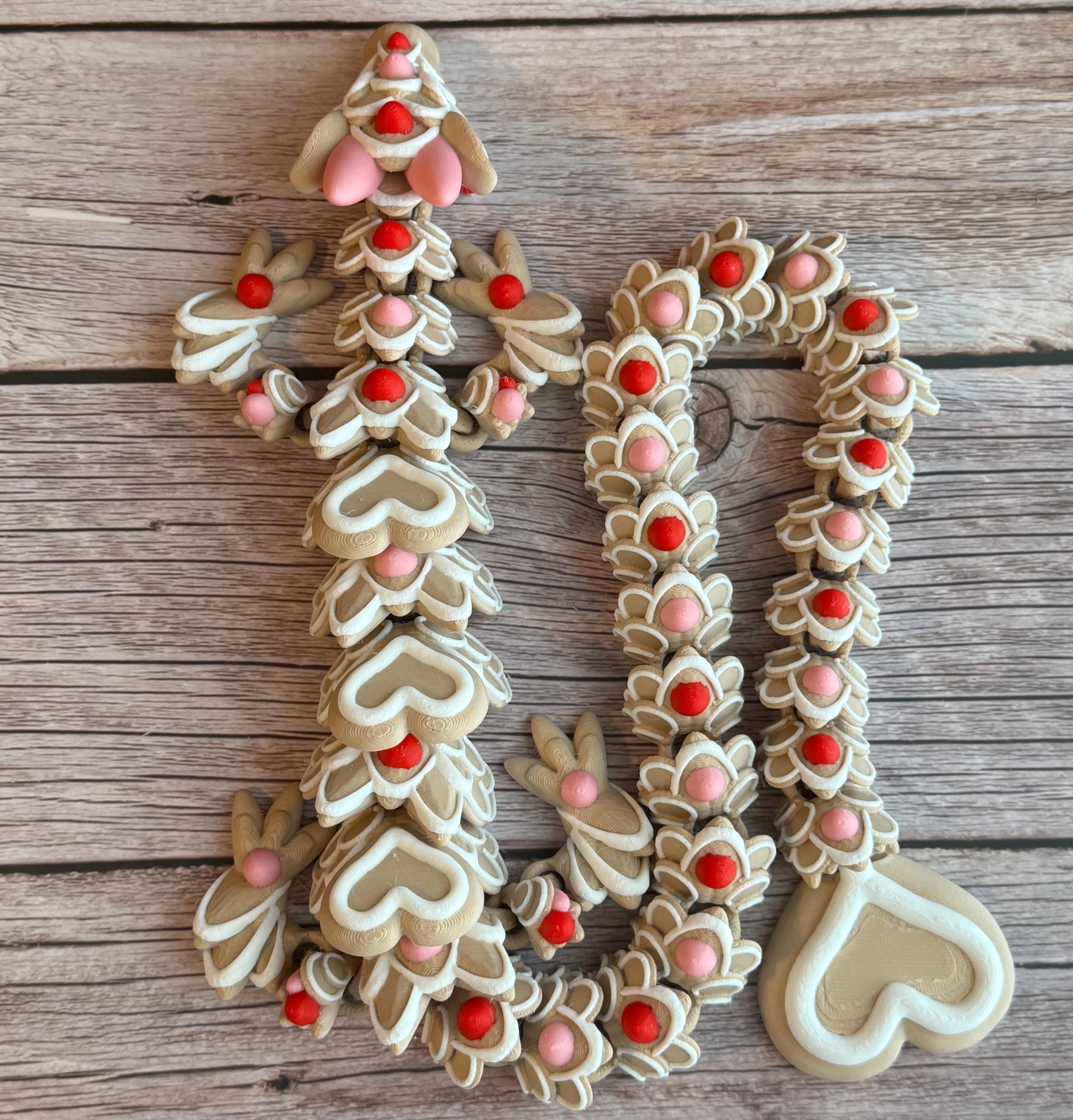 A beige colored 3D printed dragon figure with red, pink, and white heart-shaped cookie-like features, placed on a wooden surface