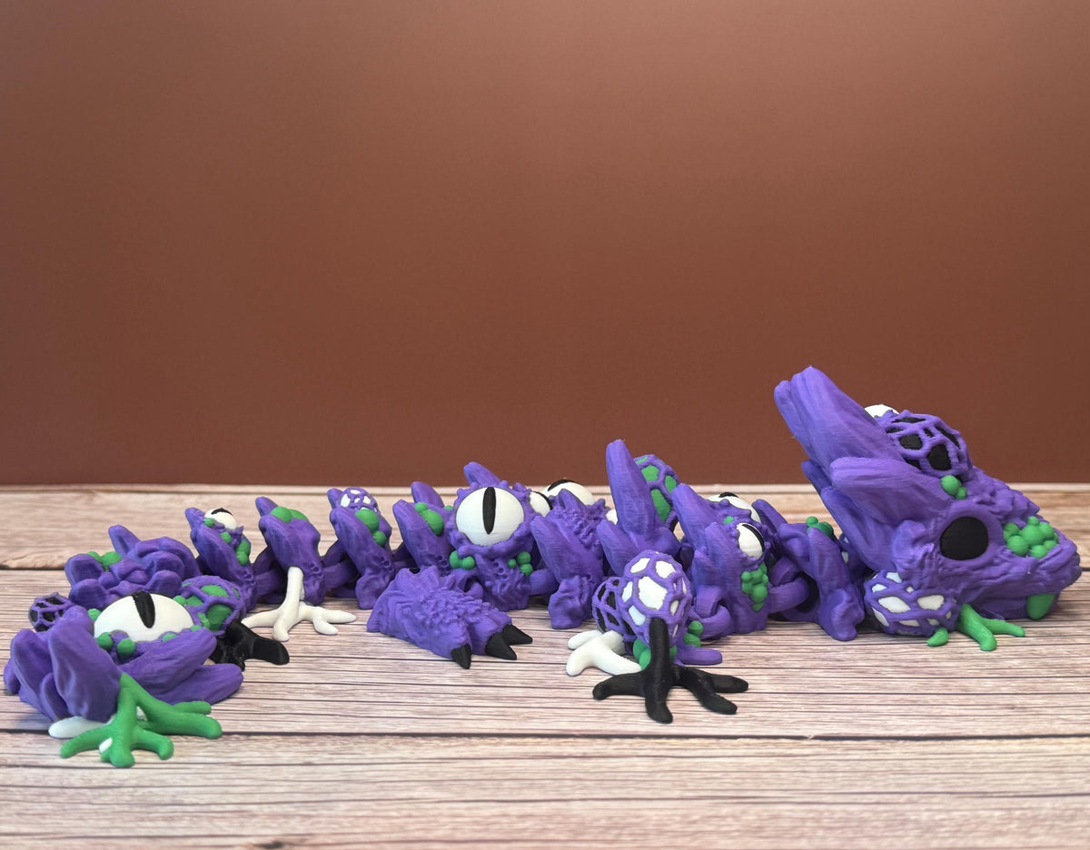 Purple and green 3D printed dragon with multiple eyes and growth-like features all over its body, placed on a wooden surface