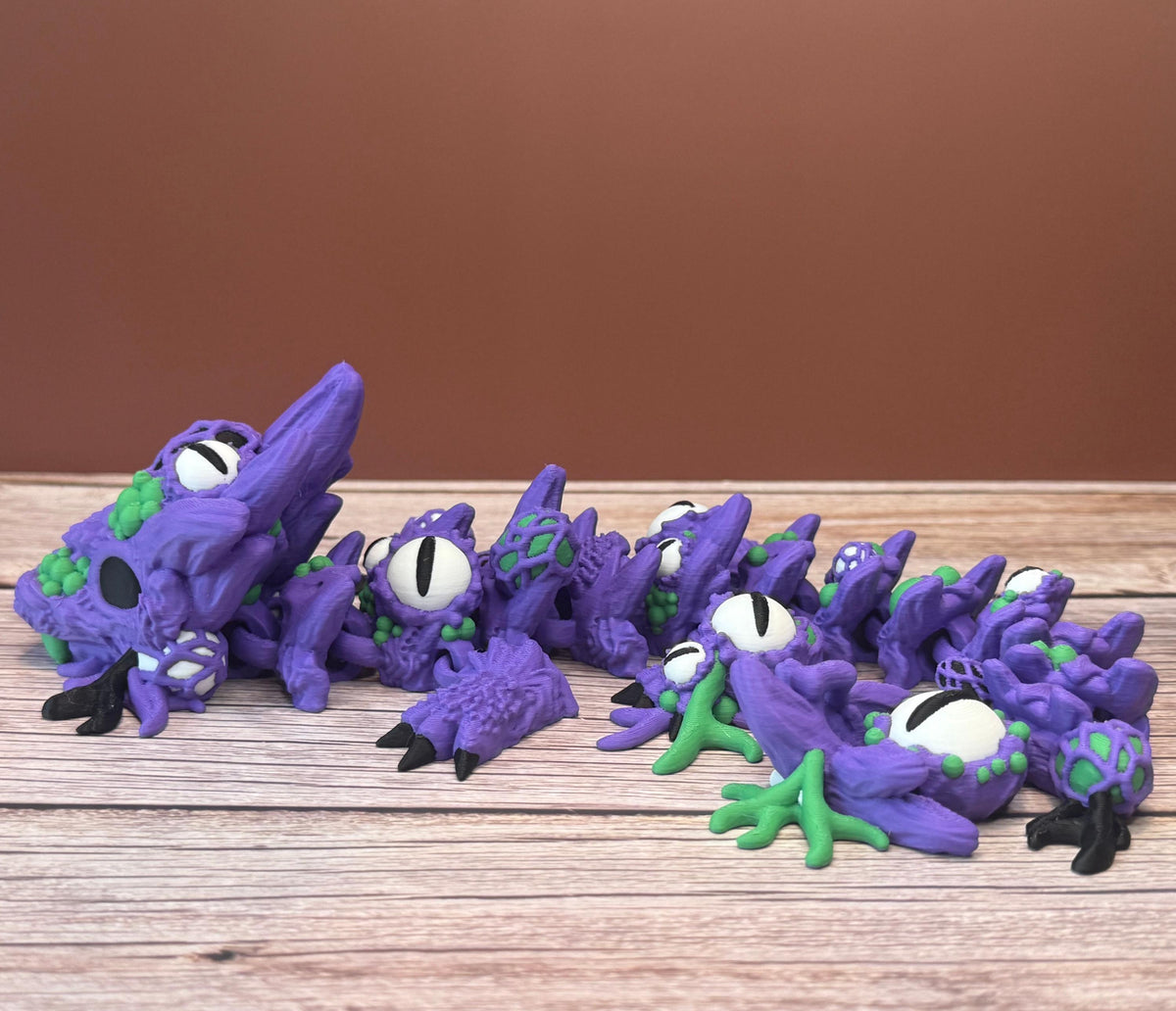 Purple and green 3D printed dragon with multiple eyes and growth-like features all over its body, placed on a wooden surface