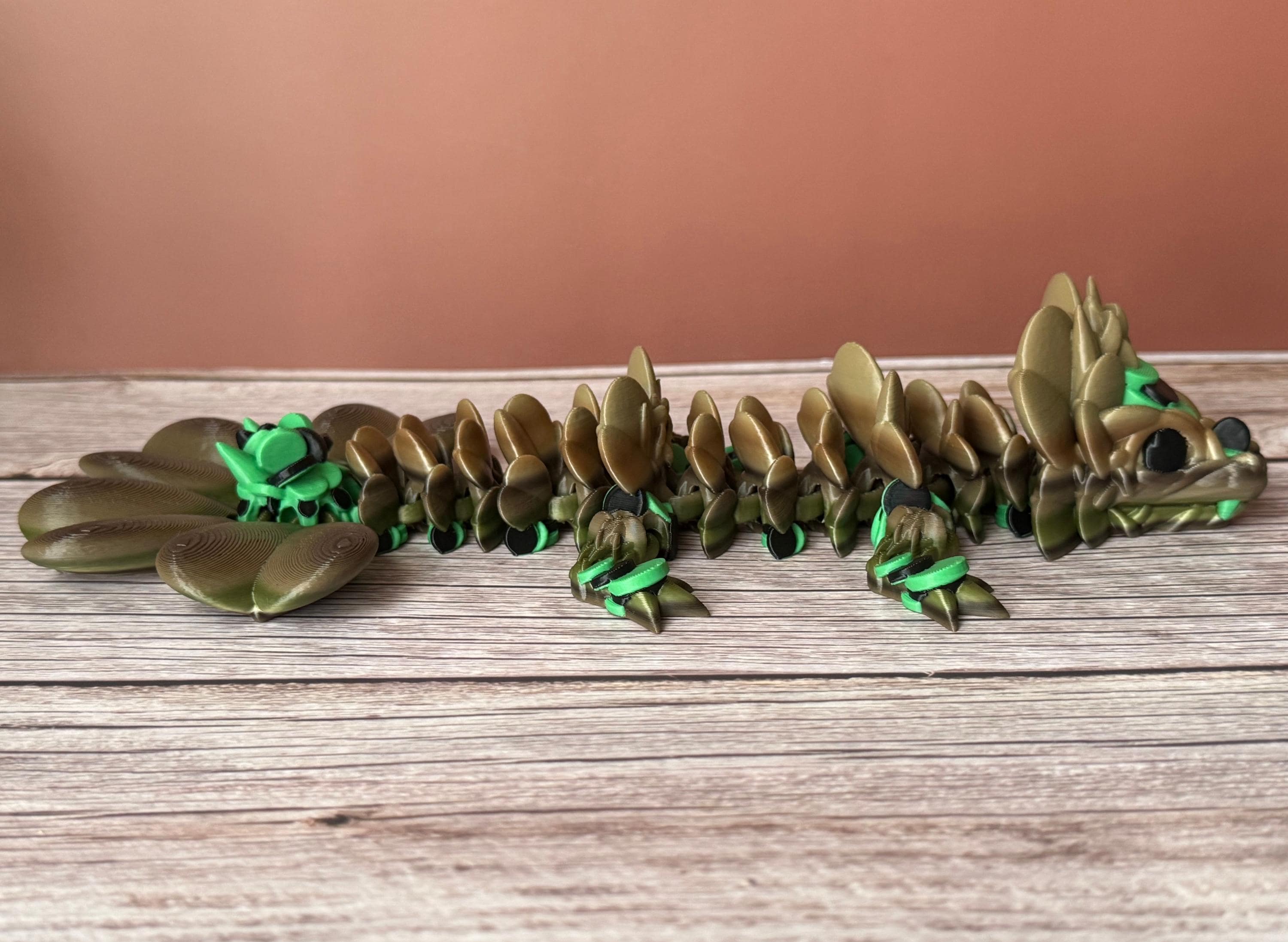 Brown and green 3D printed dragon figure with a clover shaped tail, placed on a wooden surface