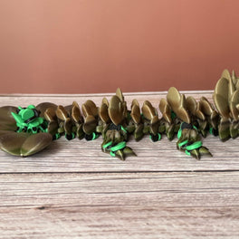 Brown and green 3D printed dragon figure with a clover shaped tail, placed on a wooden surface