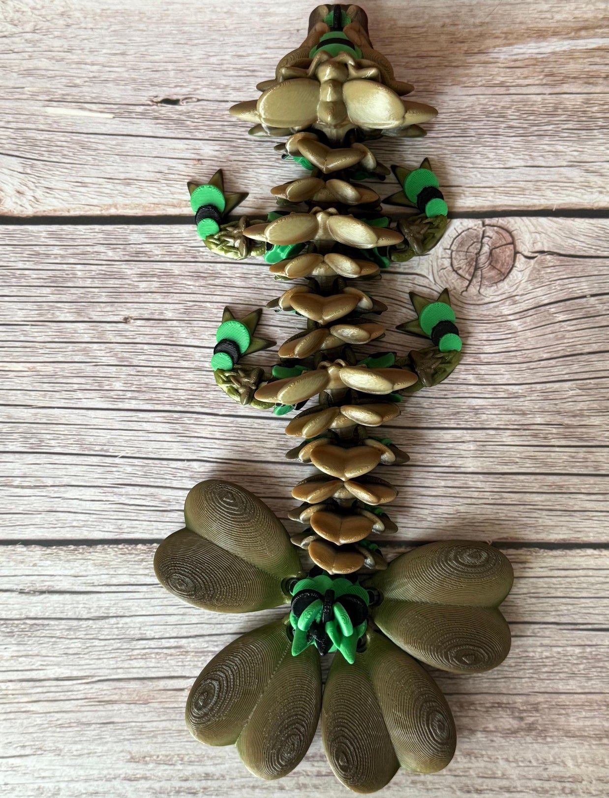 Brown and green 3D printed dragon figure with a clover shaped tail, placed on a wooden surface