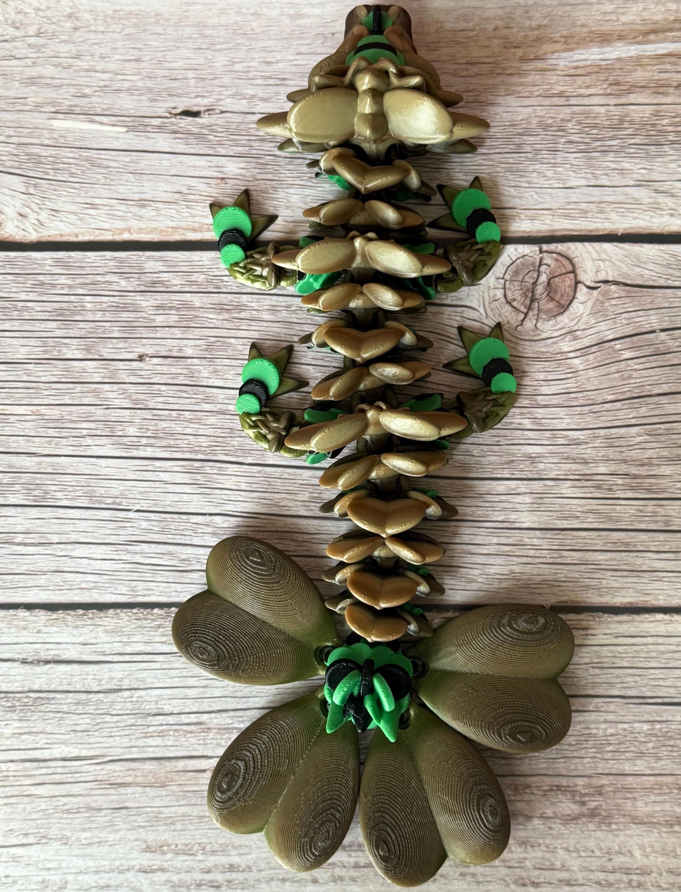Brown and green 3D printed dragon figure with a clover shaped tail, placed on a wooden surface
