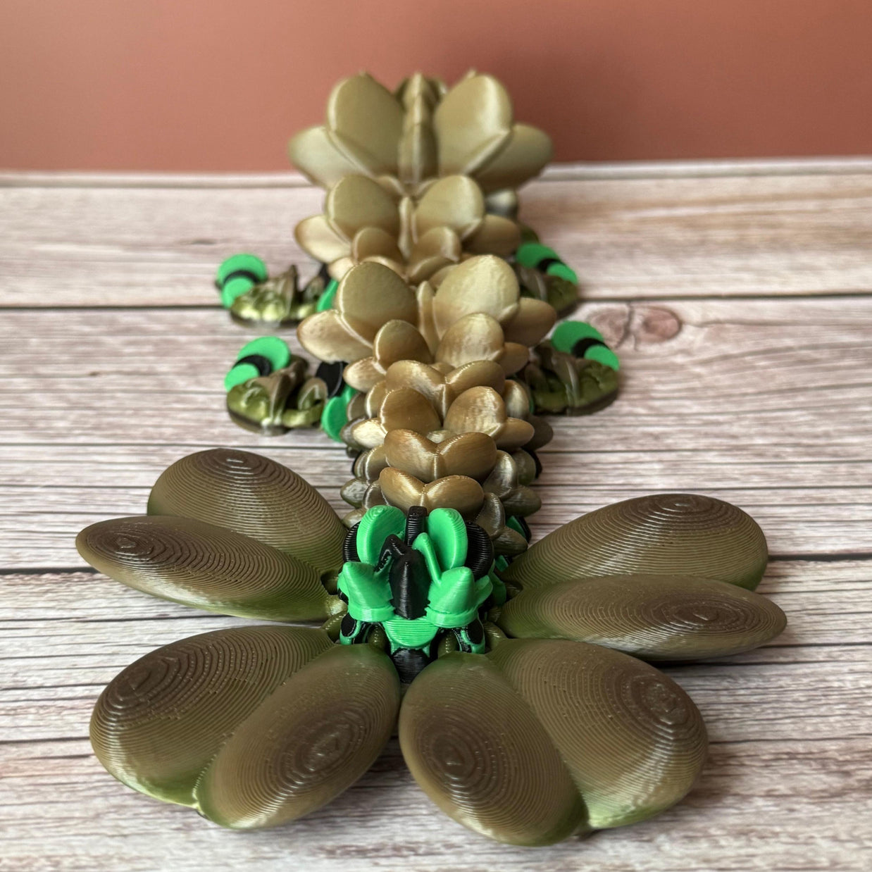 Brown and green 3D printed dragon figure with a clover shaped tail, placed on a wooden surface
