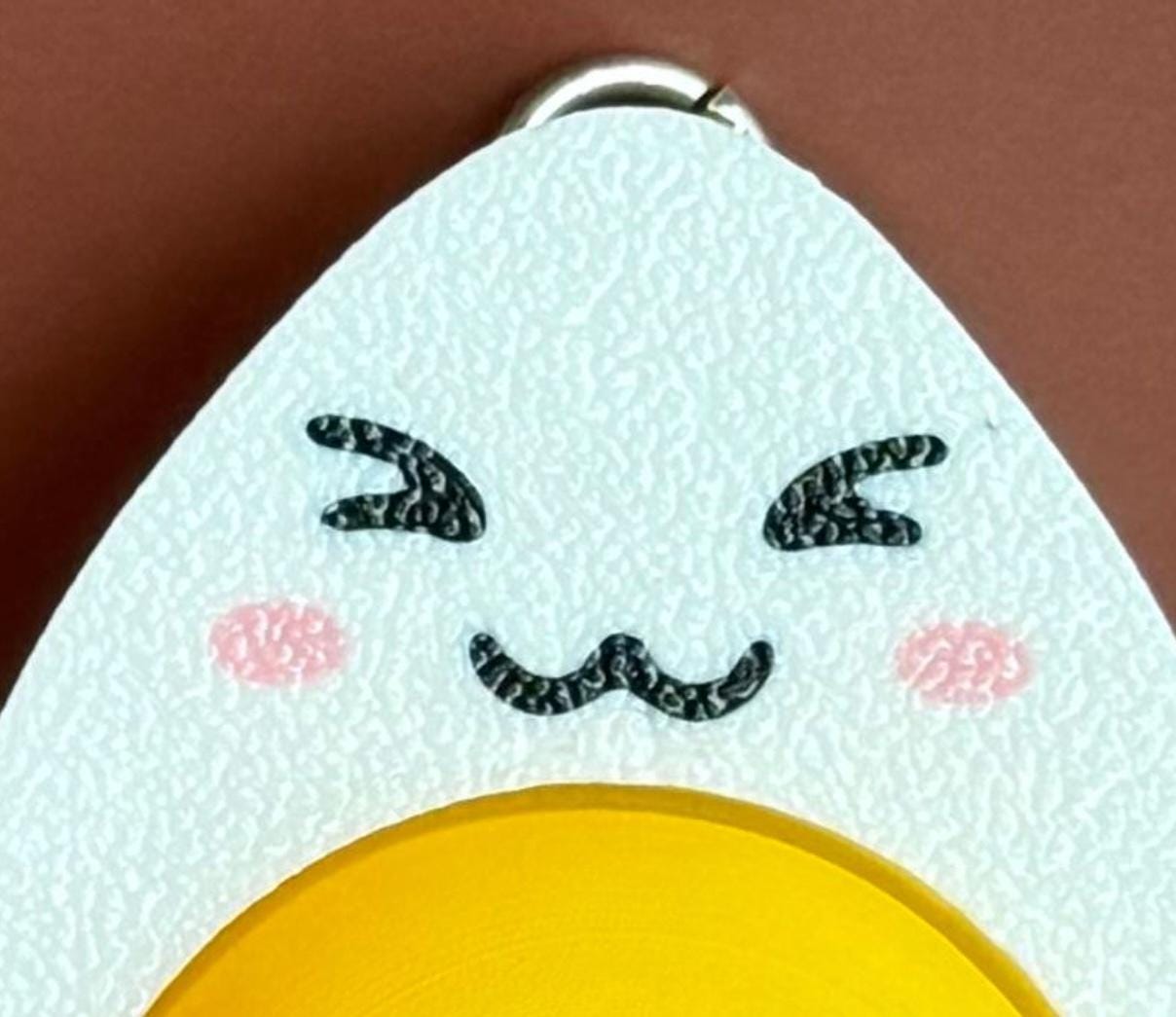 hard-boiled egg keychain with smiling face and squinting eyes, cartoonish design on a brown background