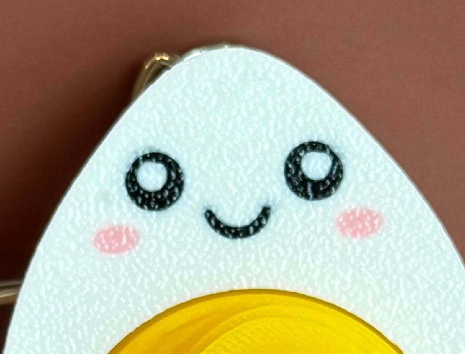 hard-boiled egg keychain with smiling face, cartoonish design on a brown background