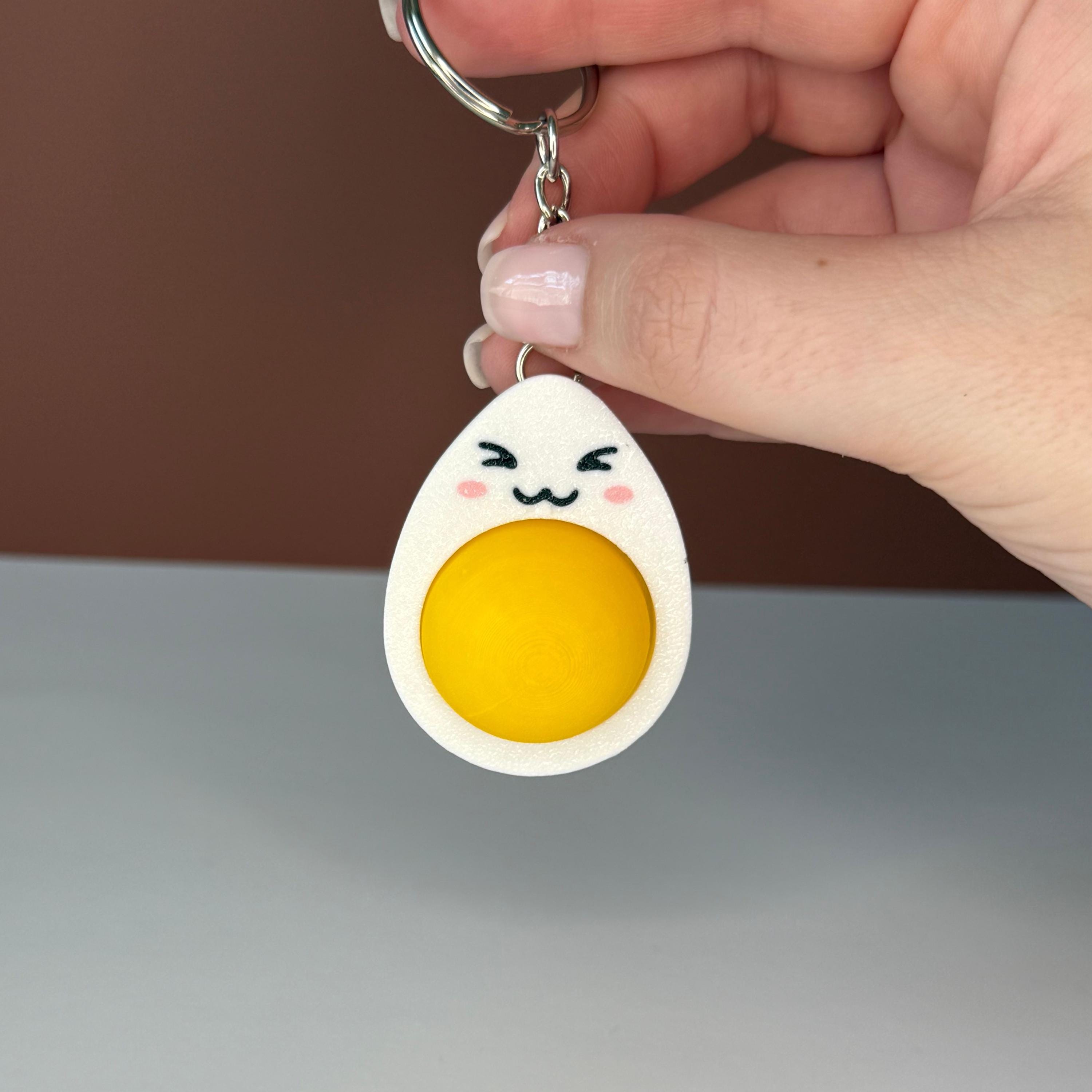 hard-boiled egg keychain with cartoonish design held by a hand against a white and brown background
