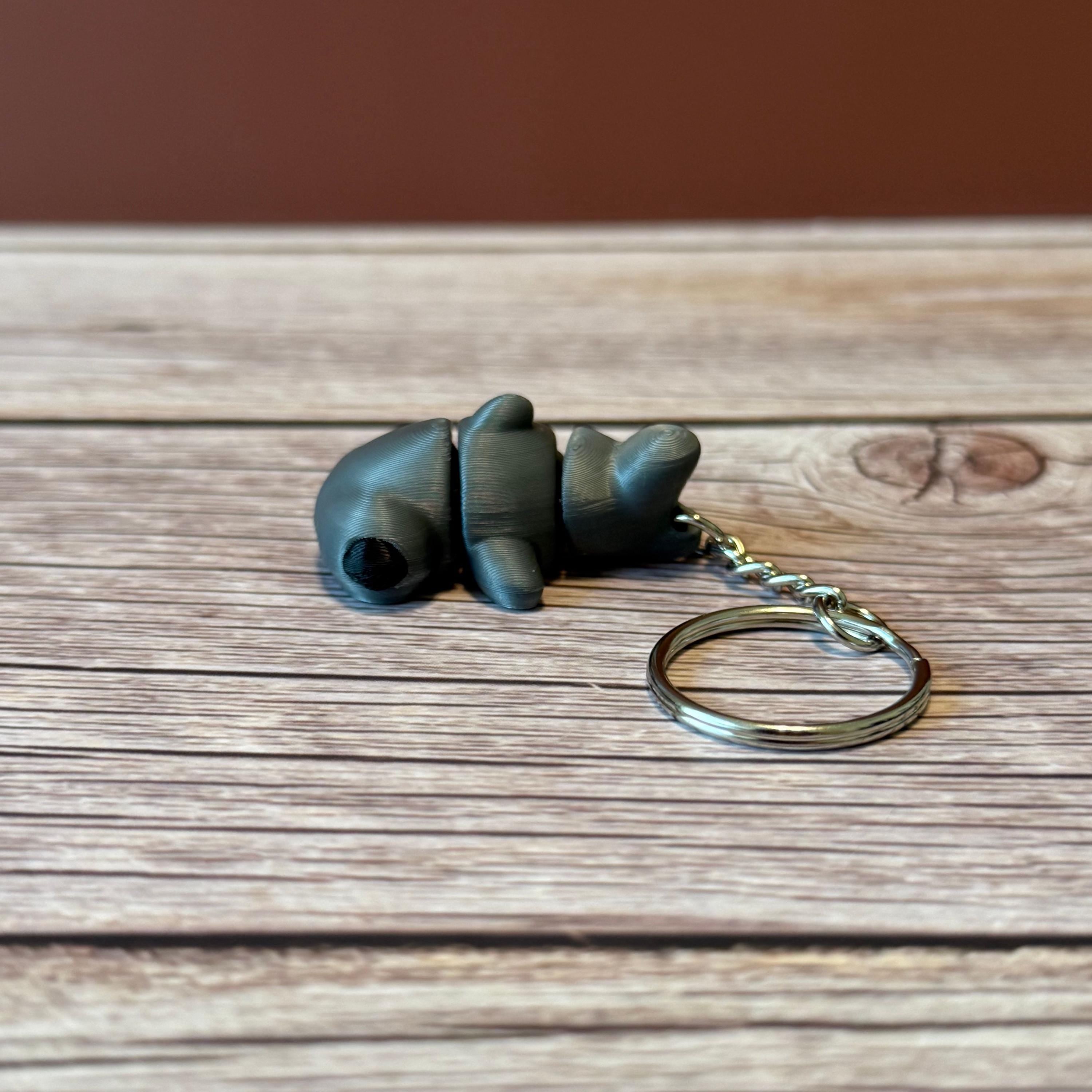 A 3D printed articulated hammerhead shark keychain in gray, displayed on a wooden surface.