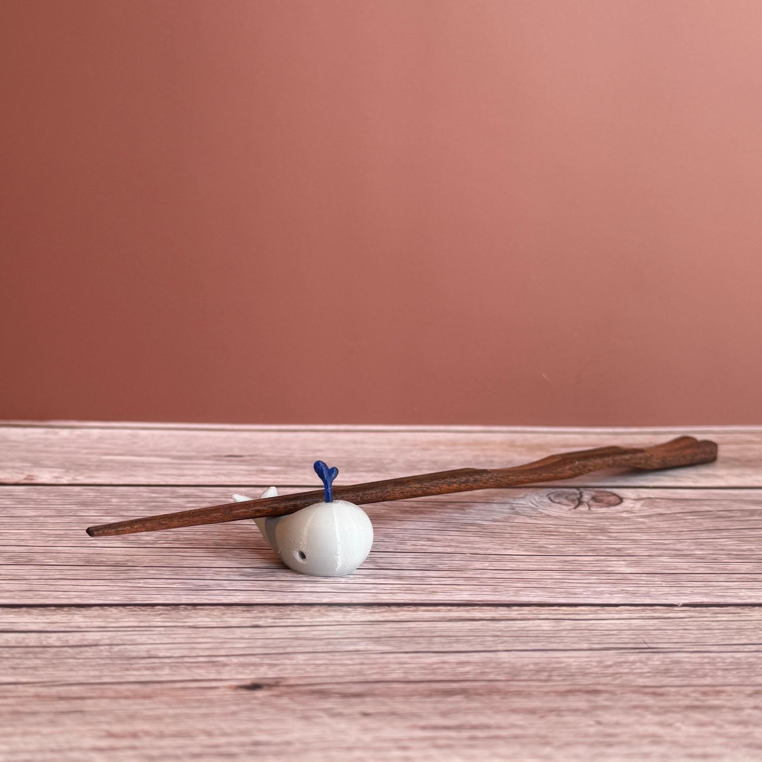 A 3D printed white whale chopstick rest with a space for holding chopsticks, placed on a wooden surface.