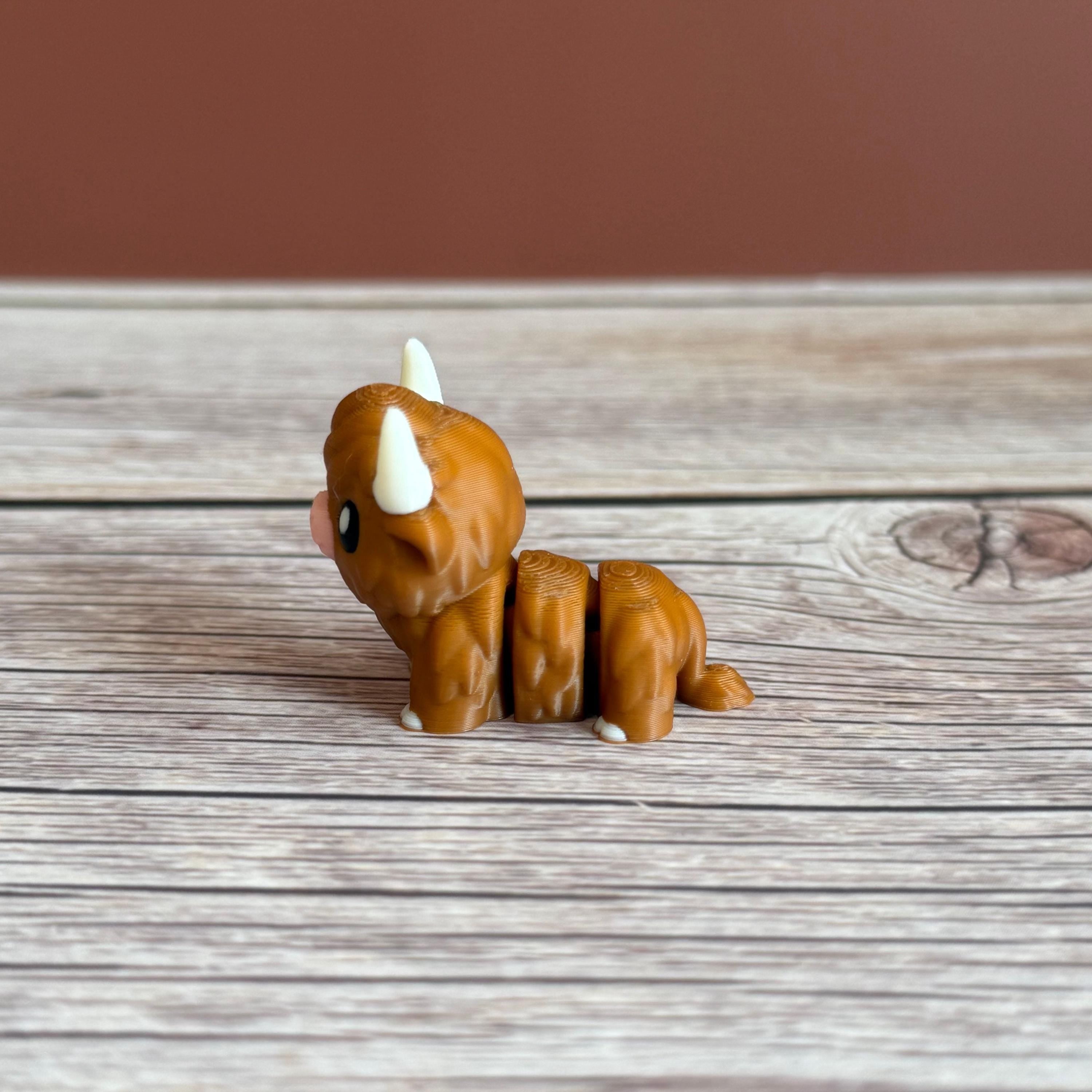 A small 3D printed articulated brown Highland cow toy with movable joints, placed on a wooden surface.