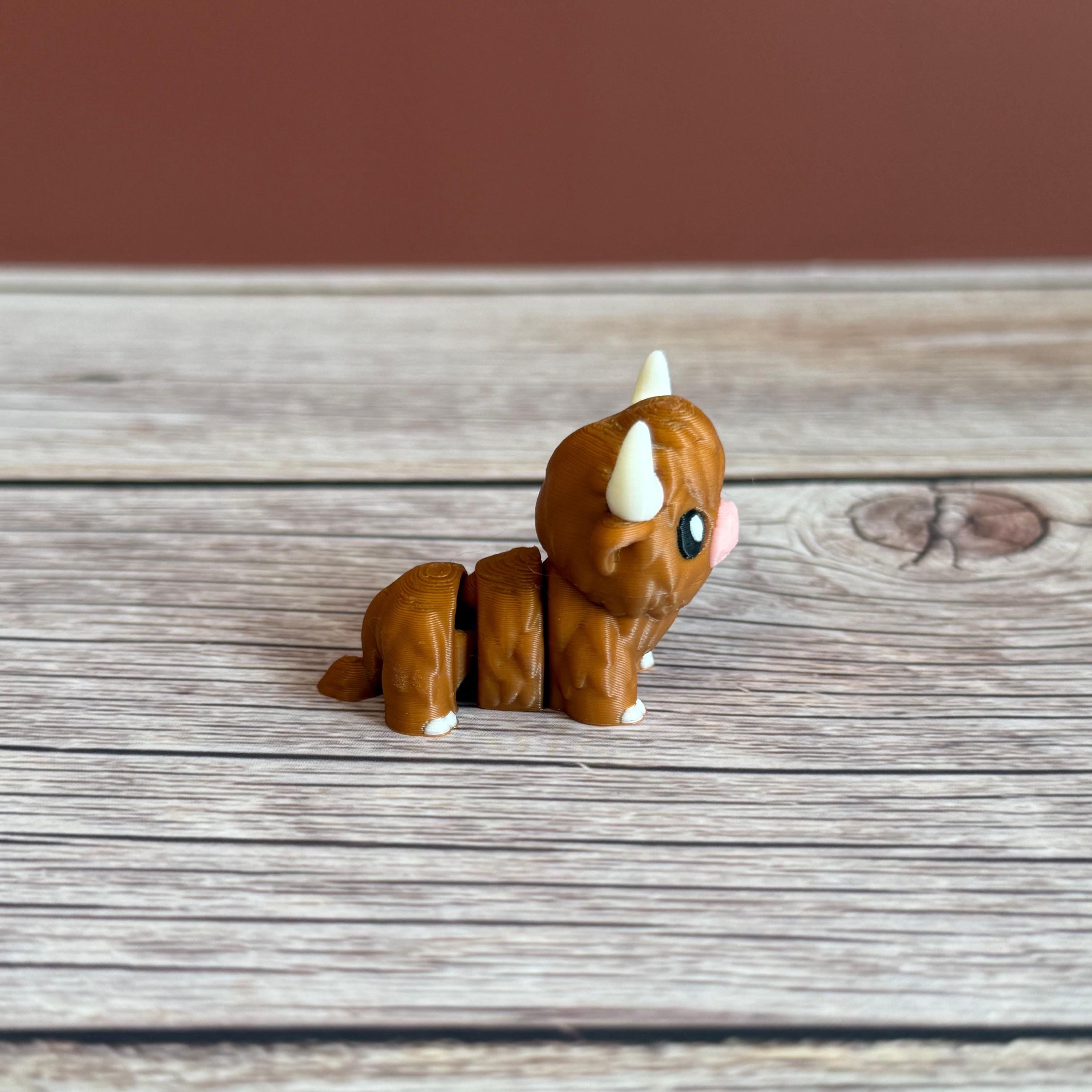 A small 3D printed articulated brown Highland cow toy with movable joints, placed on a wooden surface.