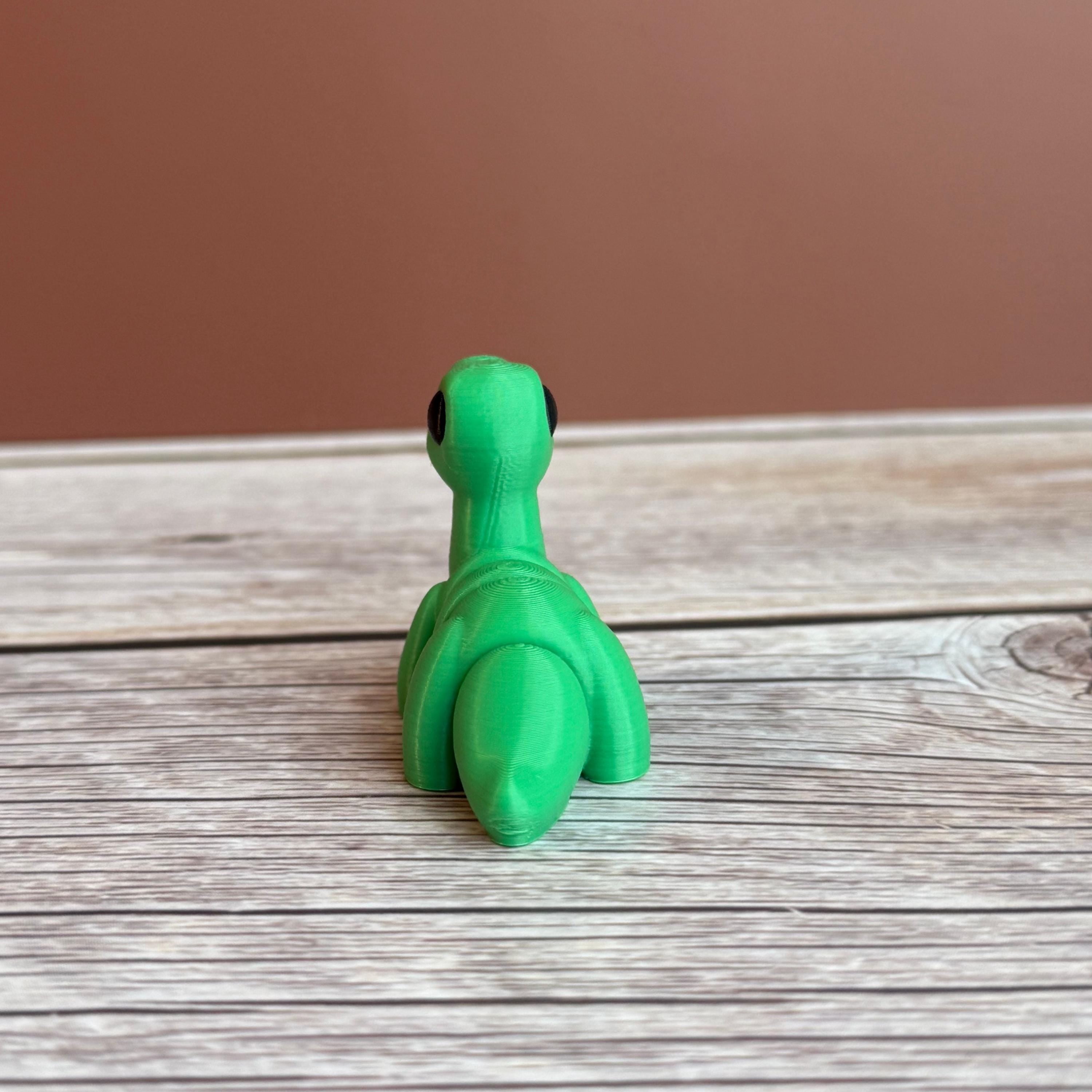 A small green 3D printed articulated Brontosaurus dinosaur toy, sitting on a wooden surface.