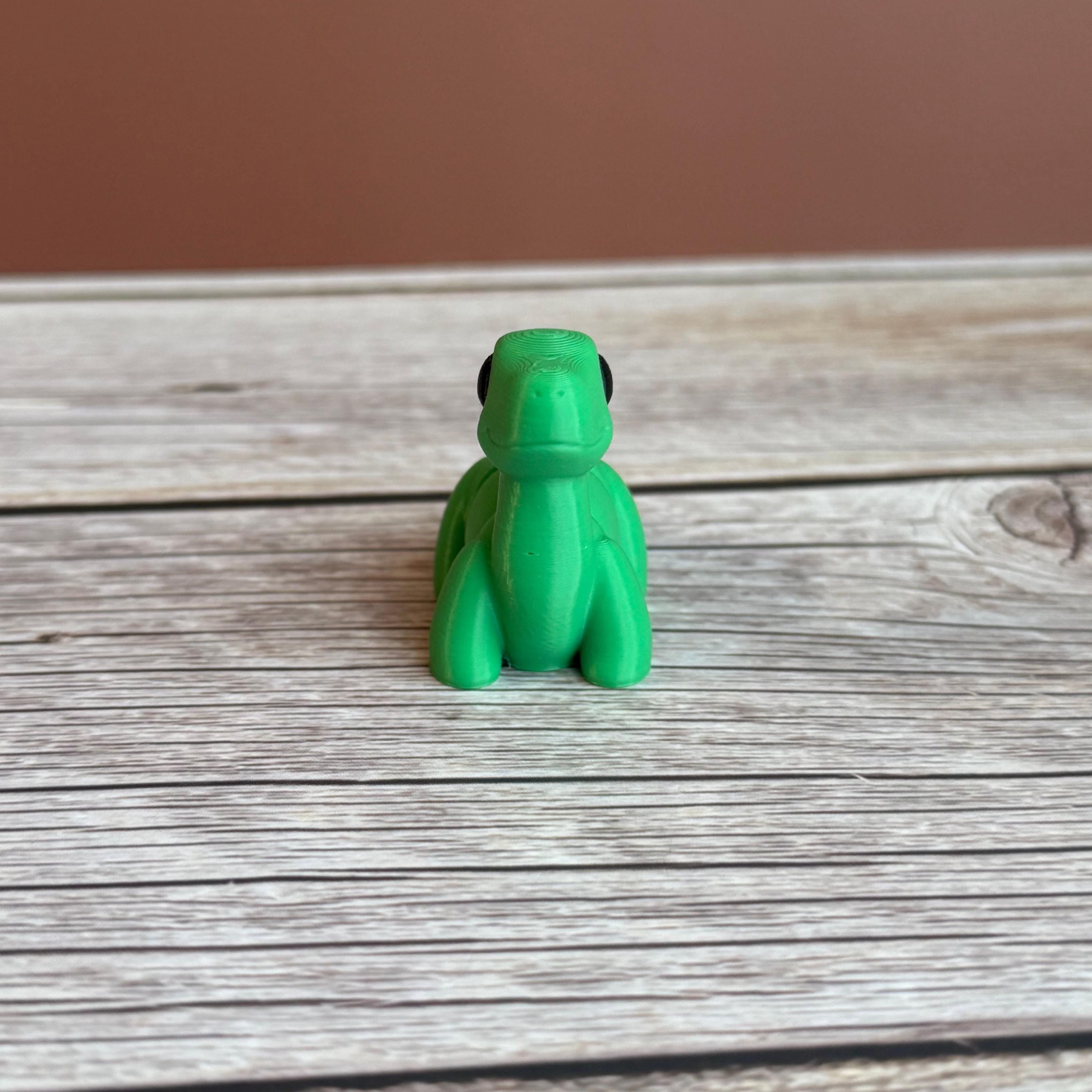 A small green 3D printed articulated Brontosaurus dinosaur toy, sitting on a wooden surface.