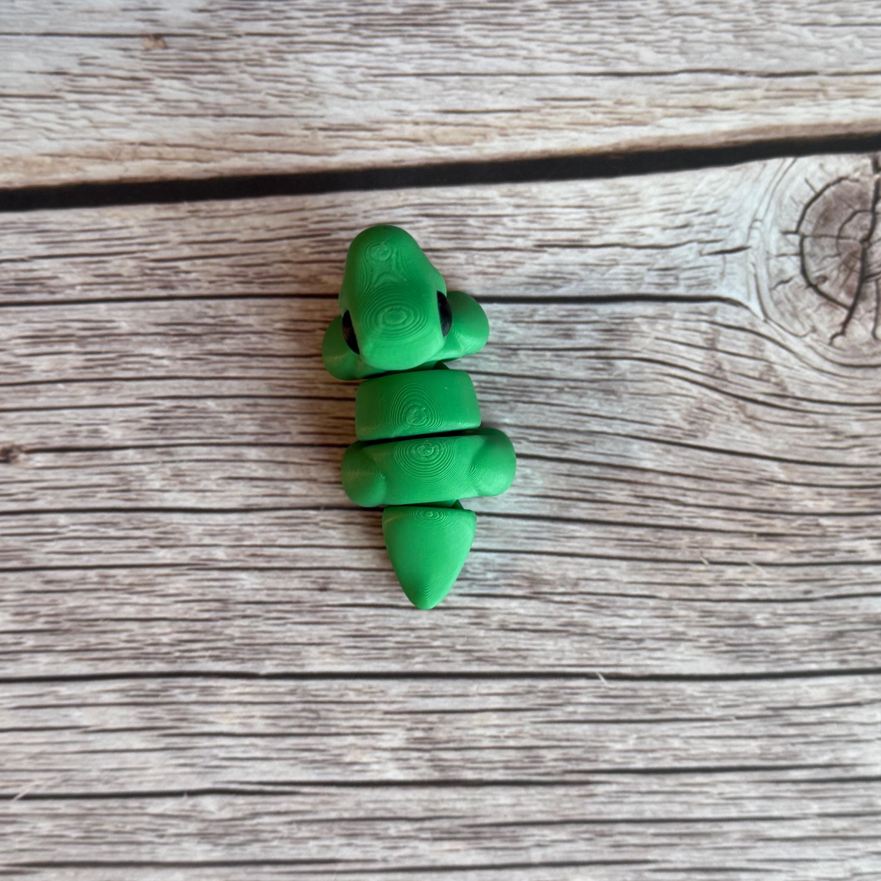A small green 3D printed articulated Brontosaurus dinosaur toy, sitting on a wooden surface.