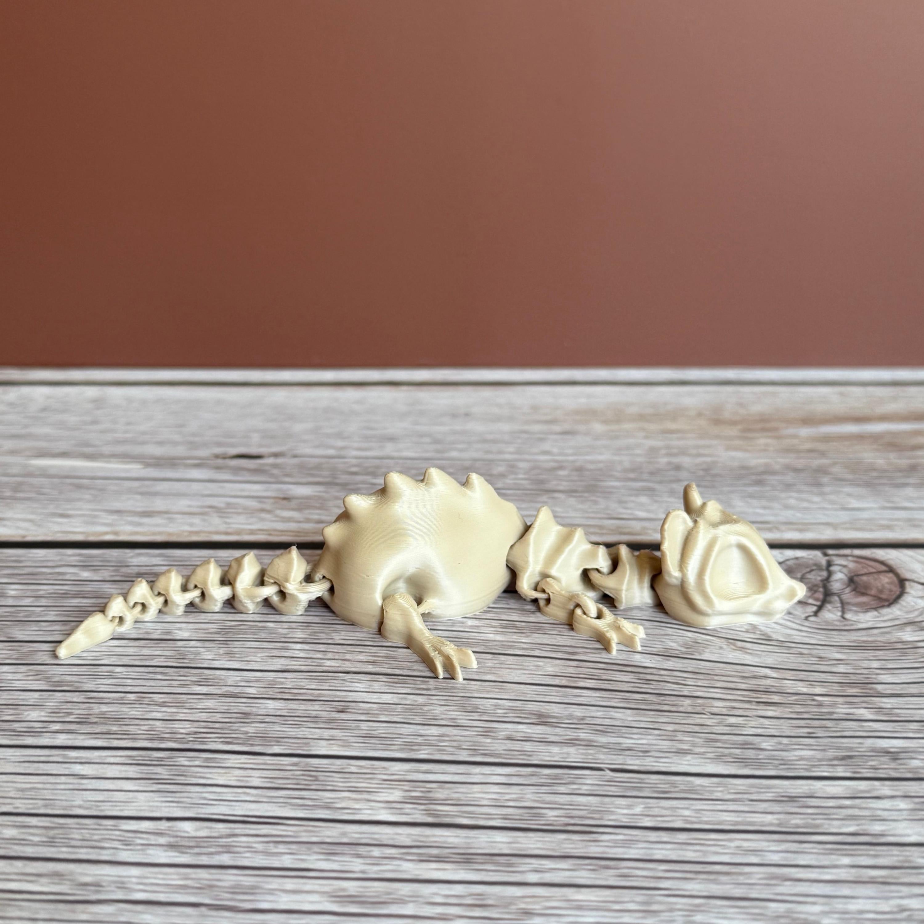 A 3D printed articulated skeleton rat on a wooden surface, with a beige color representing the bone structure.