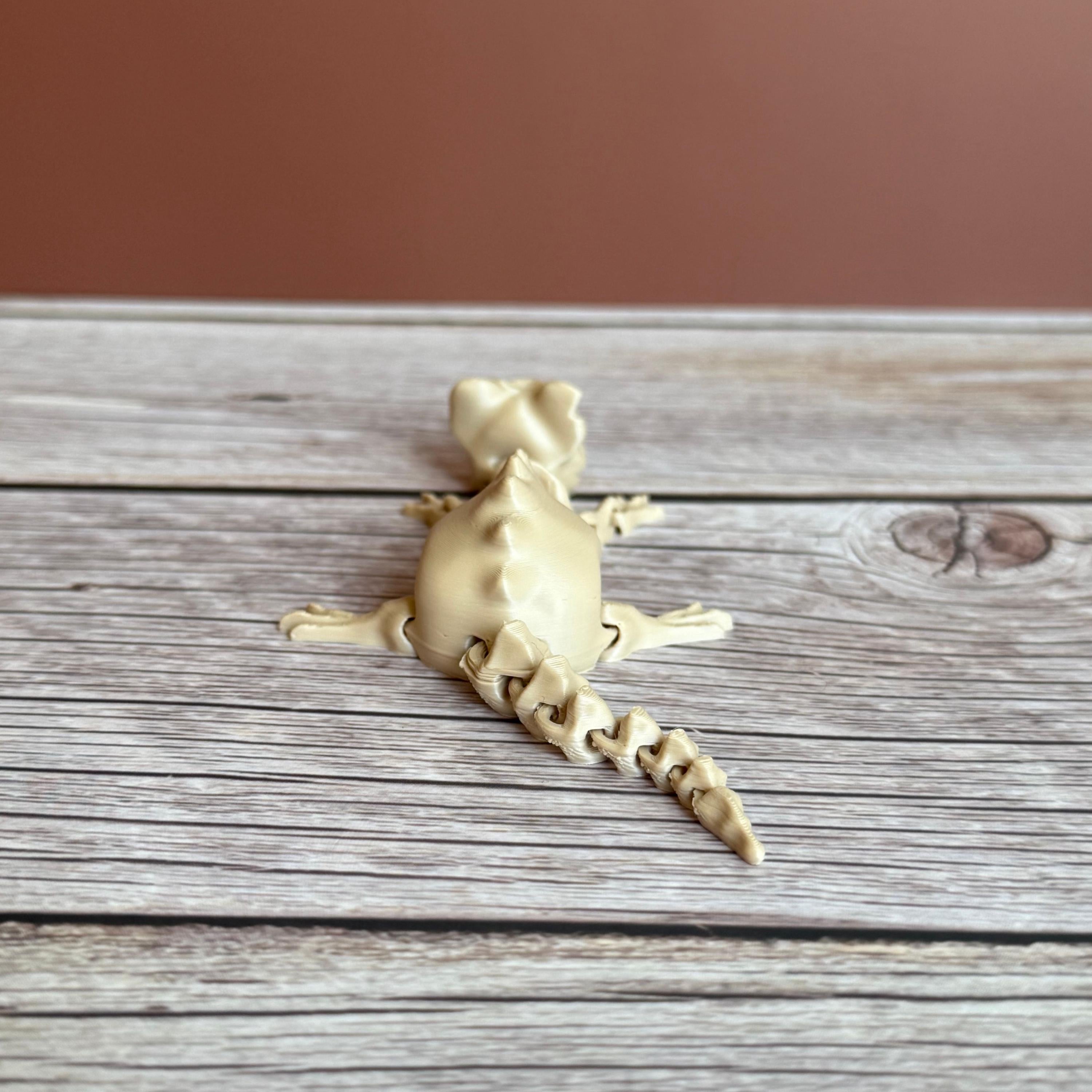 A 3D printed articulated skeleton rat on a wooden surface, with a beige color representing the bone structure.