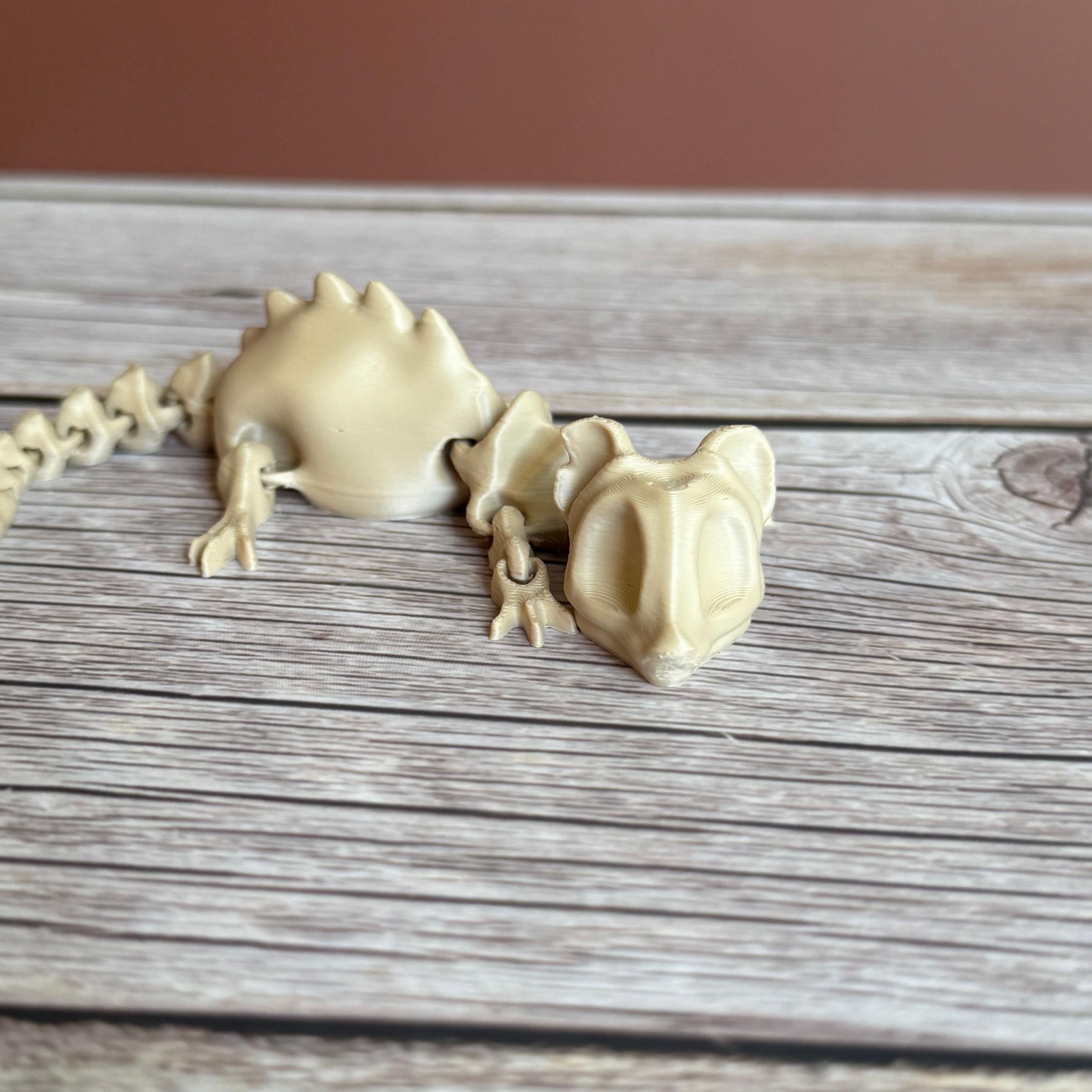 A 3D printed articulated skeleton rat on a wooden surface, with a beige color representing the bone structure.